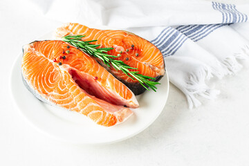 Two raw salmon steaks with peppercorn and aromatic rosemary twigs on white plate close up. Healthy food concept.