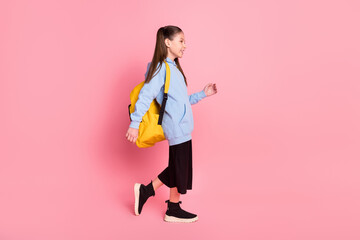 Full length body size side profile photo of small schoolgirl with yellow rucksack walking to school isolated pastel pink color background