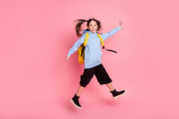 Fototapeta na wymiar Full length body size photo of small schoolgirl with yellow rucksack jumping smiling isolated pastel pink color background