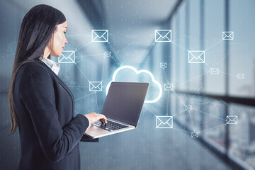 Businesswoman standing and holding a laptop with cloud holo symbol and message icons in the background, business communication and social media concept