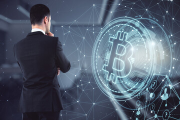 Businessman in a suit thinking and faced forward, standing in an office with big windows, bitcoin logo. Cryptocurrency and trading concept