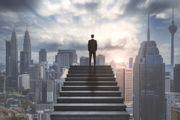 Ambition concept with confident businessman on the top of stairway and looking on city skyline - obrazy, fototapety, plakaty