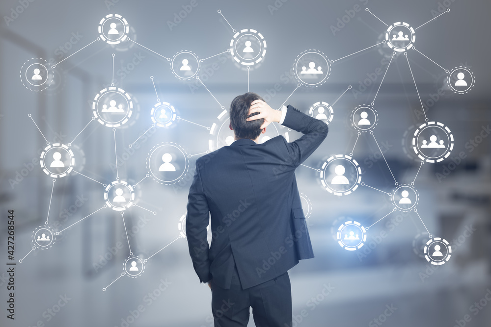 Aufkleber Puzzled businessman looking at the multiple application hologram icons with coworking space in the background. Social media and communication concept