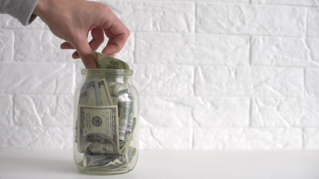 hand putting a dollar bill in a savings jar with a white label