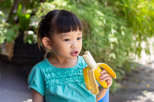 Portrait image of baby 2-3 years old. Happy Asian child girl enjoy eating a banana with sweet smiling. Food and healthy kids concept.