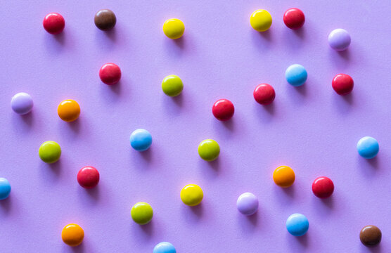 Colorful chocolate candies smarties background.Top view sweets multicolored food texture, on purple background.