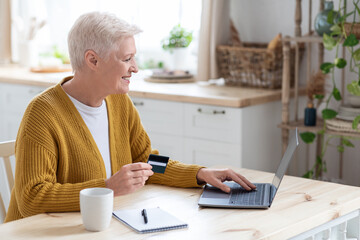 Happy aged lady holding credit card and using laptop