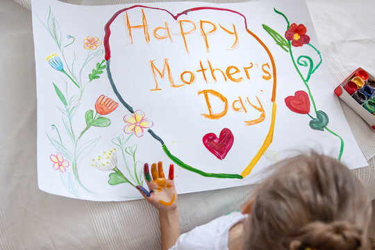 A little girl draws with paints a festive greeting card for mother's day.