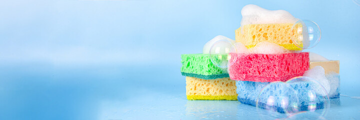 Spring home cleaning, housekeeping concept, Set of various bright detergent washing rubber sponges for cleaning, with lush foam and soap bubbles on a blue background top view copy space - obrazy, fototapety, plakaty