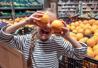 Funny little girl with oranges in the supermarket.