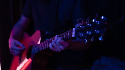 Naklejka premium Close up of a guitarist playing an acoustic guitar in colored lighting.