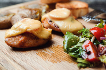 Baked chicken fillet with cheese, baked potatoes and salad on a wooden board. Quick dinner dish recipe.