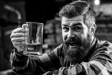 Beer pub. Bearded hipster holds glass of beer. Handsome positive man drinks beer at pub.