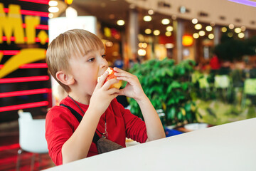 Cute kid eating apple in modern cafe. Happy and healthy childhood. Funny boy with apple, sitting at the table.