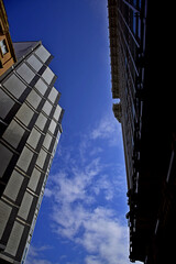 Fototapeta premium Imagen de ángulo bajo que marca el contraste entre las fachadas de dos edificios, uno moderno y otro antiguo, dejando ver en medio el azul del cielo