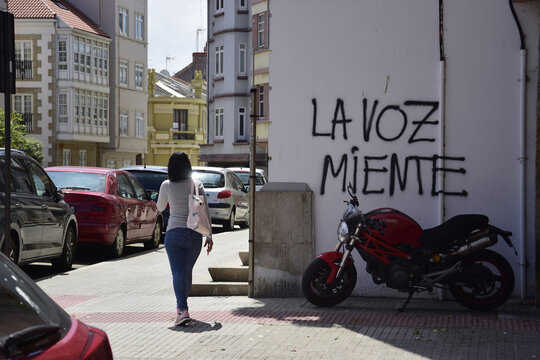Una mujer de espaldas pasa junto a una pintada callejera en la que se lee el juego de palabras "La Voz miente"