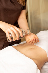 Obraz na płótnie Canvas Massage of the abdomen with oil. Anticellulite massage. Masseuse holds a transparent bottle of oil