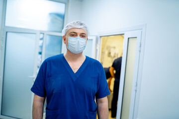 Fototapeta na wymiar Doctor in blue uniform and mask standing near operating room. Man in hospital.