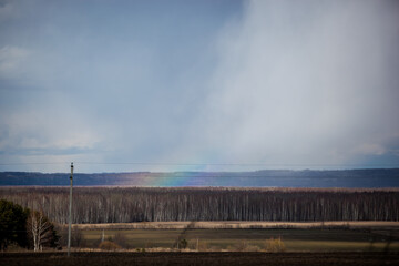 a piece of rainbow against the background of thunderclouds and spring fields