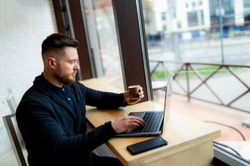 Attractive handsome businessman working on distance in a cafe. Young male have a coffee break after work.