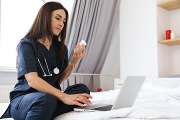 Focused woman doctor holding medicine while working with laptop