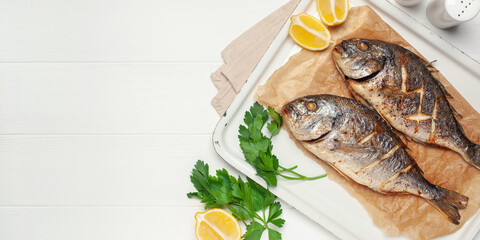 Baked dorado fish with lemon and parsley in a dish on the table. Top View