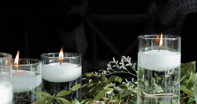 Beautiful wedding table d&eacute;cor flat lay of white floating lit candles in vases and green plants.
