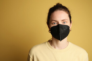Young woman in black face mask isolated on yellow background. 