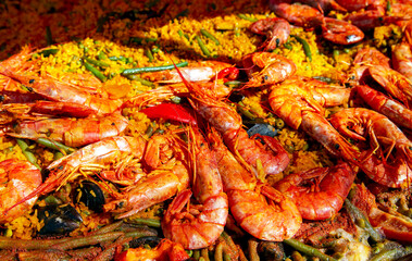 Spanish paella with green beans, large prawns and other seafood cooked in a wok pan on the street. 