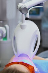 Teeth whitening in a dental clinic.Bleaching with cold light.The concept of health and beauty.The person is out of focus.Close-up.Ultraviolet light.Vertical photo.