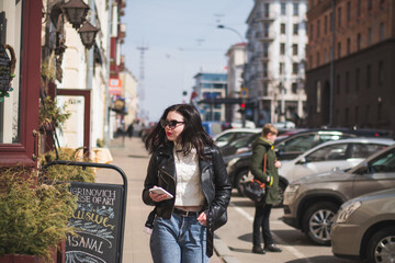 Fototapeta na wymiar Young cheerful stylish woman using cell phone and texting message on city street