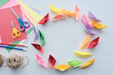many multi-colored boats. View from above. DIY origami boat. Scissors, plain pencil, colored paper. Crafts for children, creativity. Light background.