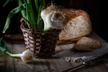 Fresh green onions in a wicker basket and bread on a rustic table