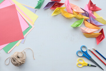 many multi-colored boats. View from above. DIY origami boat. Scissors, plain pencil, colored paper. Crafts for children, creativity. Light background.