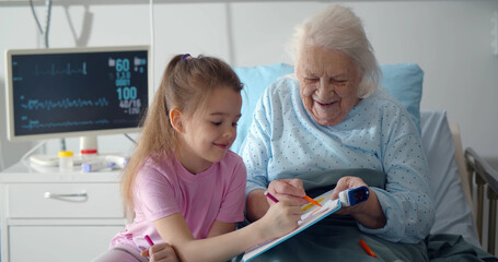 Little girl visiting grandmother in hospital bed painting together