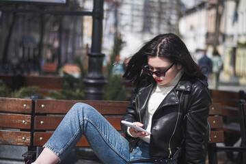 Young cheerful stylish woman using cell phone and texting message on city street