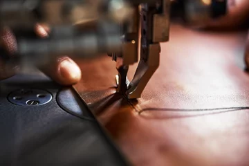 Deurstickers Working process of leather craftsman. Tanner or skinner sews leather on a special sewing machine, close up.worker sewing on the sewing machine © Georgii