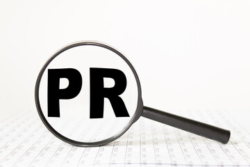 words PR in a magnifying glass on a white background. business concept