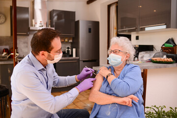 Fototapeta premium elderly senior woman with surgical mask having covid 19 vaccine injection by doctor male nurse at home