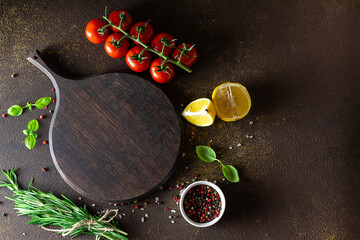 Wooden cutting board with herbs, vegetables and spices on dark background. Copy space for your design.