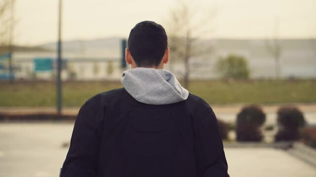 Hombre con chaqueta negra y capucha caminando de espaldas ,  hombre mirando hacia atr&aacute;s y luego camina hacia su moto