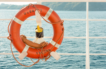 An orange lifebuoy attached to the railing of a ship or ferry against the backdrop of the blue sea...