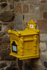 Ein alter gelber gußeisener Briefkasten befestigt an einer Steinwand.
