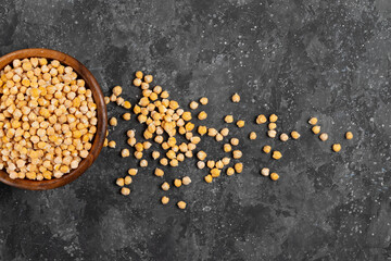 Raw chickpeas in a wooden eco friendly plate on a gray napkin with grains scattered on the table
