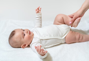 Newborn healthy baby doing physical exercises for the legs and hip joint. With the help of the medic's mom. On white background.