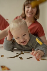 Mom and son rejoice at the holiday and lie on the floor. Happy mom and son throw gold tinsel. Holiday. Body positive