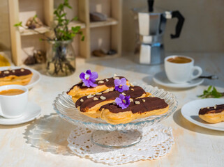 Dessert, choux pastry sweets with vanilla custard, covered with chocolate glaze, on a glass stand on a light concrete background. French cuisine.