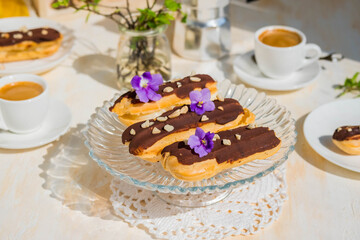 Dessert, choux pastry sweets with vanilla custard, covered with chocolate glaze, on a glass stand on a light concrete background. French cuisine.