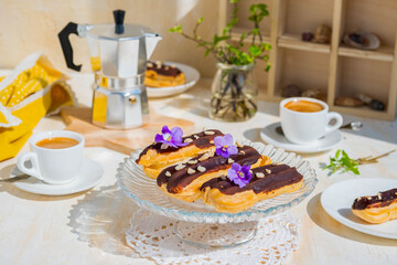 Dessert, choux pastry sweets with vanilla custard, covered with chocolate glaze, on a glass stand on a light concrete background. French cuisine.