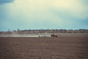Fototapeta na wymiar Farm tractor plows the field and prepares for sowing